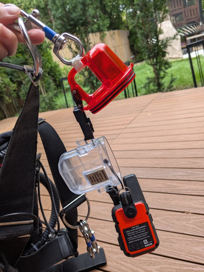 The inReach Mini secured inside its dive case by a lanyard, with the case itself clipped to the harness by a separate carabiner.