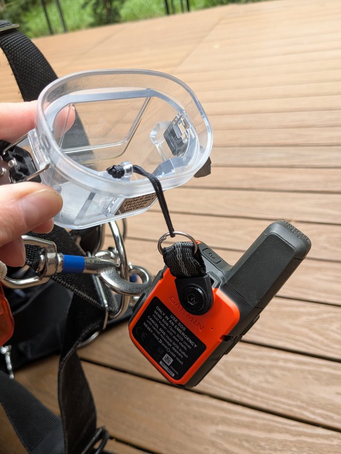 A hand opening the SOS button cover on the dive case, with the inReach Mini's emergency instructions visible.
